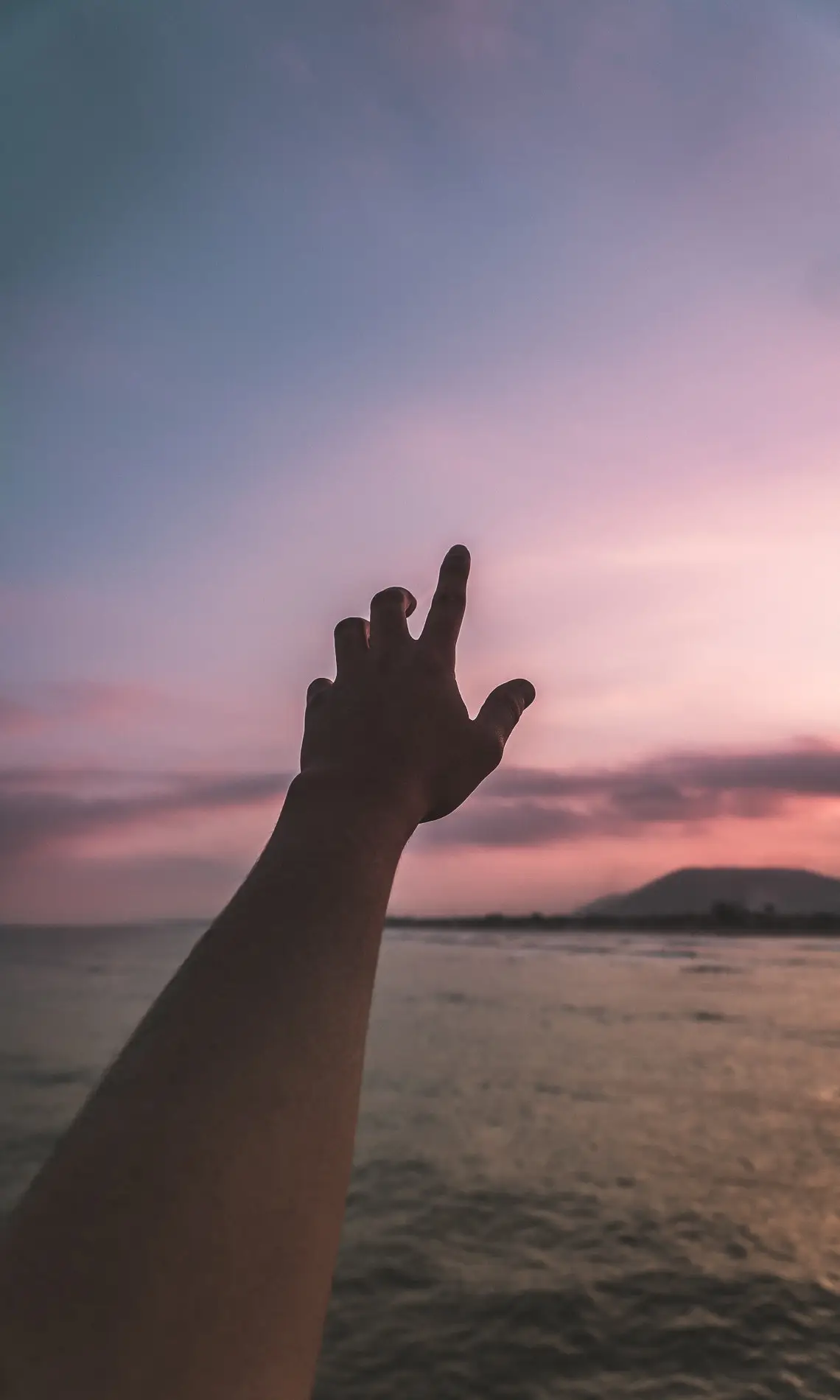 A hand is reaching for the sky at sunset.